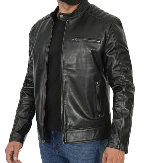 A man wearing a black leather biker jacket with a stand collar, zippered chest pocket, and zippered side pockets, styled over a black shirt and blue jeans against a white background.