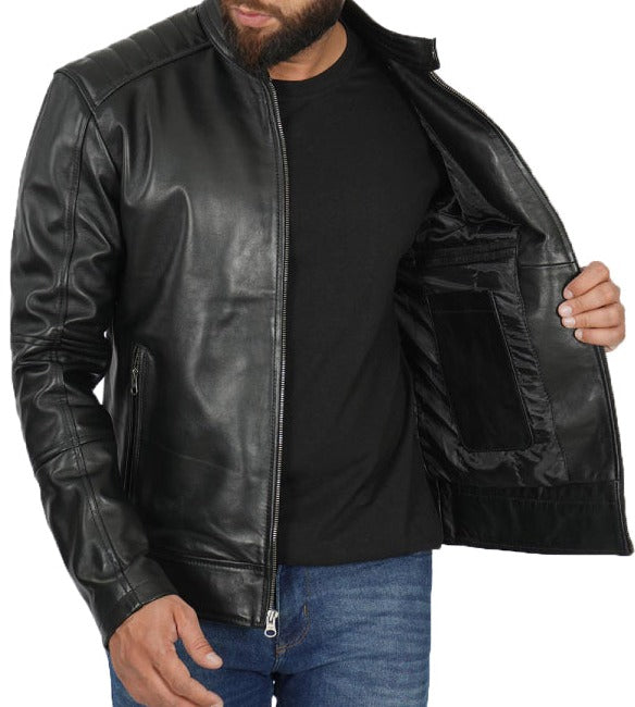 A man wearing a black leather jacket over a black t-shirt and blue jeans, holding the jacket open to show the interior lining and pocket.