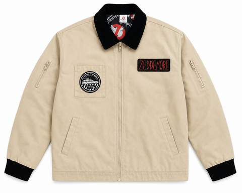 A beige zip-up jacket with a black collar, black cuffs, and black pocket trim. It features a circular patch on the left chest and a rectangular patch on the right chest that reads 'ZEDDEMORE' in red letters.