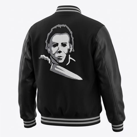 Black leather-look varsity jacket shown from the back, featuring a large white and gray graphic of Michael Myers holding a knife across the back, with striped ribbed collar, cuffs, and hem on a light gray background.