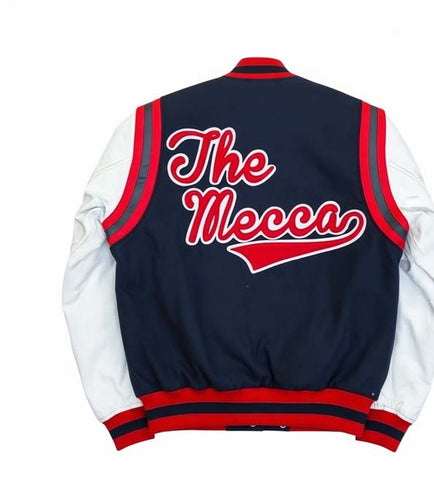 Back view of a varsity-style jacket with a navy blue body, white sleeves, and red and navy ribbed trim. Large red script text reading 'The Mecca' is printed across the back.