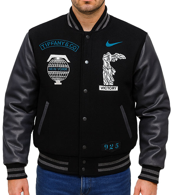 A black varsity-style jacket with black leather sleeves, featuring embroidered graphics including a Tiffany & Co. logo, a Nike swoosh, and a Statue of Liberty patch on the chest.