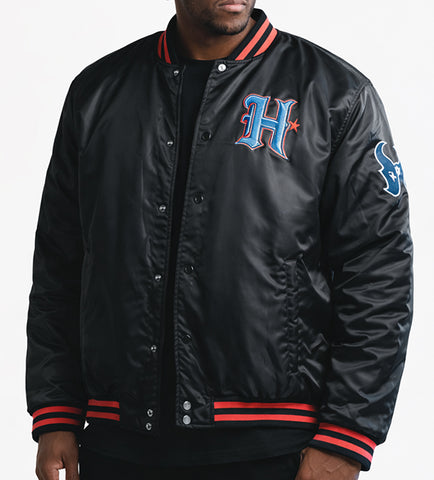 A black satin bomber jacket with red and white striped ribbed trim, featuring a blue and red embroidered 'H' logo on the left chest and a Houston Texans patch on the right sleeve, worn by a model.