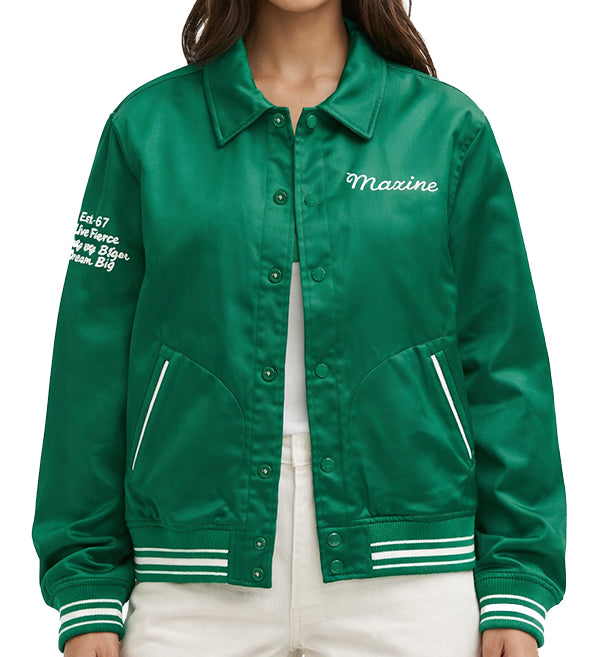 A green satin varsity-style jacket with white embroidered text reading 'Maxine' on the chest and white text on the sleeve, worn by a model over a white top and white pants against a plain white background.