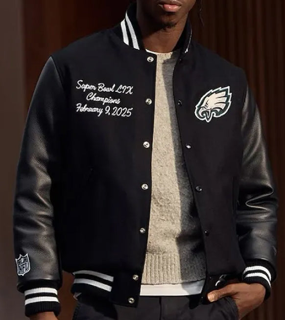 A man wearing a black varsity-style jacket with leather sleeves, white striped ribbed trim, and Philadelphia Eagles branding. The jacket features custom Super Bowl LIX championship embroidery on the left chest and an NFL shield logo on the right sleeve.