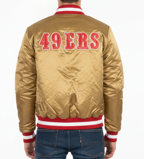 A man viewed from the back wearing a shiny gold satin bomber jacket with '49ERS' in red letters outlined in white on the back, red and white striped ribbed collar, cuffs, and hem, paired with blue jeans.