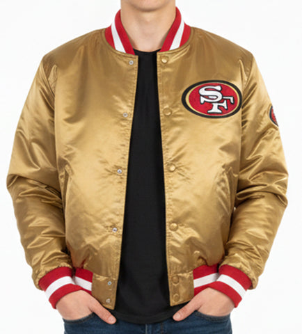A man wearing a shiny gold satin bomber jacket with red and white striped ribbed collar, cuffs, and hem. The jacket features the San Francisco 49ers logo on the left chest.